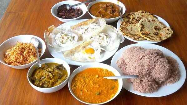 A variety of dishes including curry, rice, and flatbreads on a wooden table. - YKC Holdings (Katugastota)