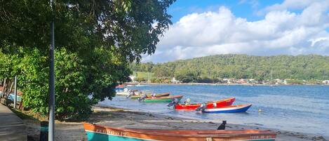 A beach with several boats moored on the sand, a clear sky, and a distant view of a hill with vegetation.