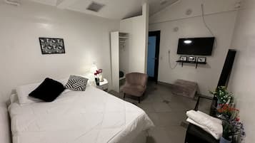 A bedroom with a bed, bedside table, lamp, chair, TV, and a small table with flowers.