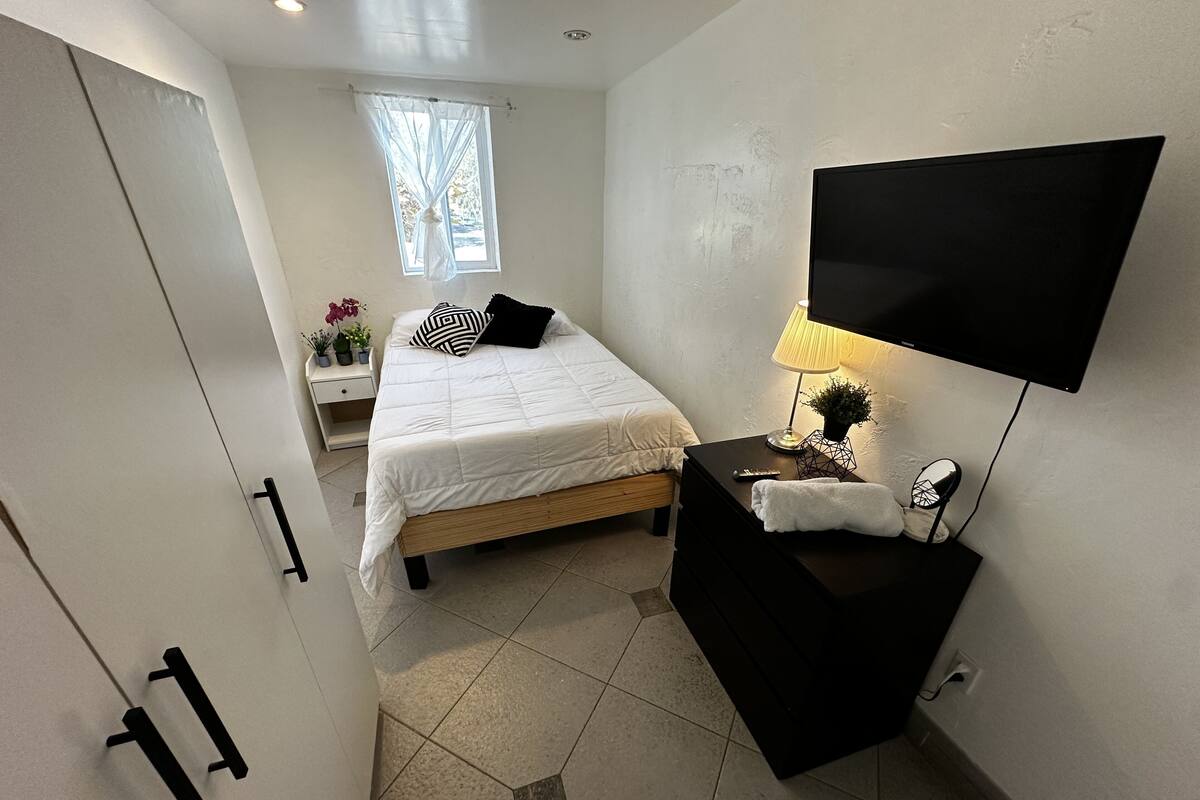 Ein Schlafzimmer mit einem Bett, einem Nachttisch, einer Lampe und einem an der Wand befestigten Fernseher.