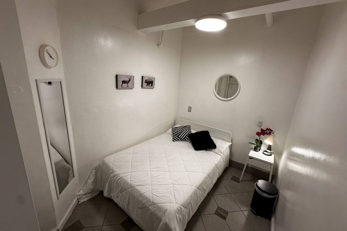 Ein Schlafzimmer mit einem Bett, einem runden Spiegel, einer Uhr und zwei gerahmten Bildern an der Wand.