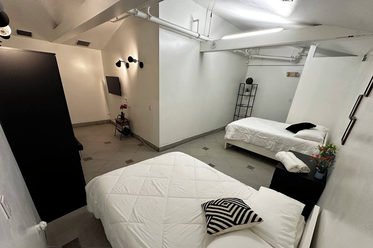 Ein Hotelzimmer mit einem Bett, einem Schreibtisch, einem Sessel, einem kleinen Tisch mit Pflanze und einem an der Wand befestigten Regal.