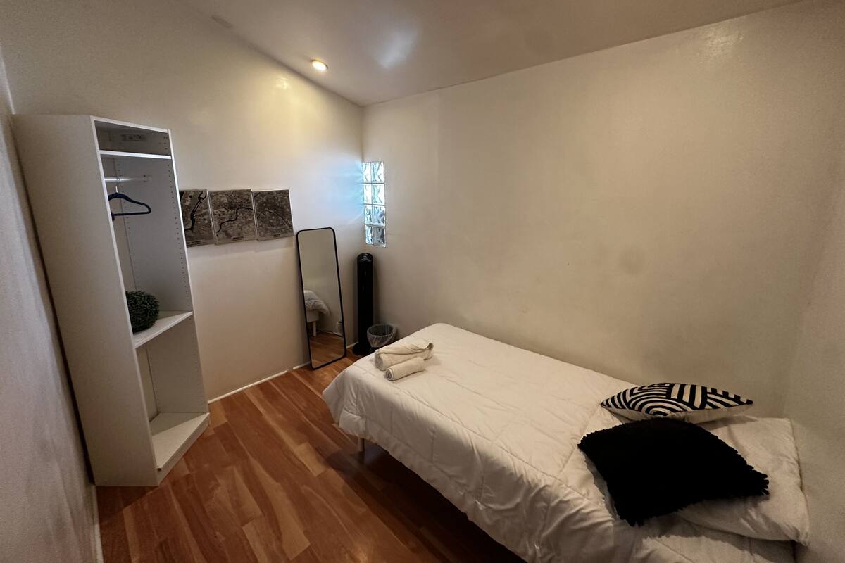 Ein Schlafzimmer mit einem Bett, einem Kleiderschrank, einem Spiegel und einem kleinen Fenster.