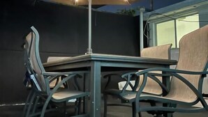 An outdoor patio area with a table and chairs, an umbrella, and string lights. - Culver City Hostel (Culver City)