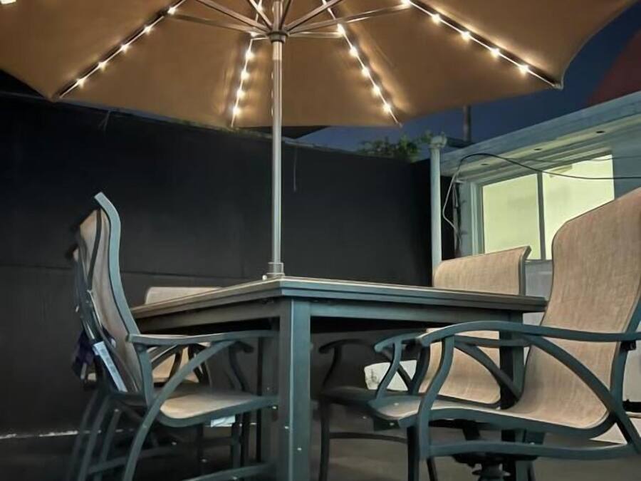 Uma área de varanda externa com mesa, cadeiras, um guarda-sol e luzes de fada.