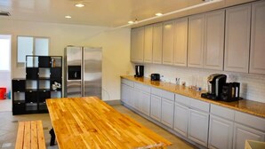A modern kitchen with grey cabinets, a stainless steel refrigerator, a wooden table, and a coffee maker. - Culver City Hostel (Culver City)