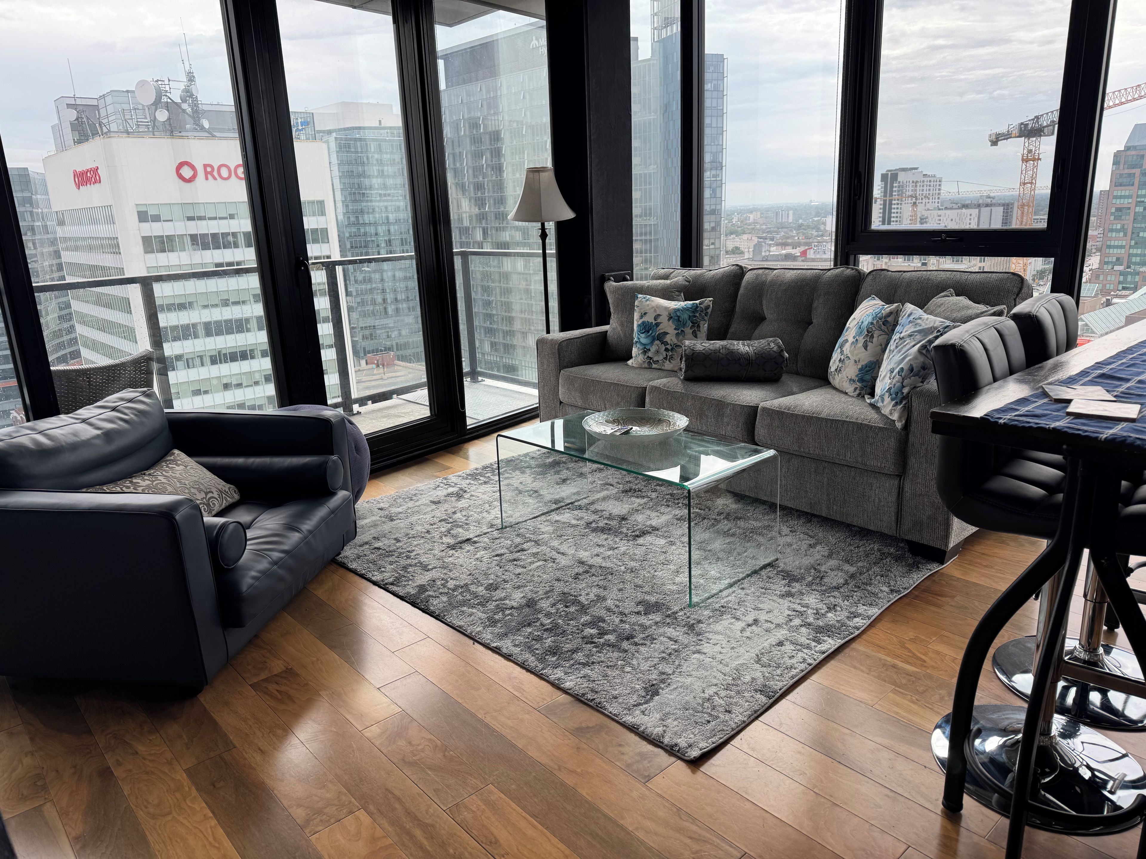 A modern living room with a glass coffee table, grey sofa, and a view of city buildings.