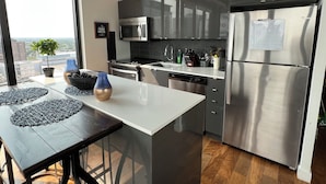 A modern kitchen with stainless steel appliances, a white countertop, and a view of the city through large windows. - 18th floor 2 bed 2 bath overlooking downtown  (Winnipeg)