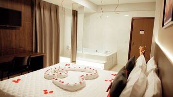 Quarto de hotel com cama, escrivaninha, cadeira, televisão, banheiro com banheira e porta com placa.