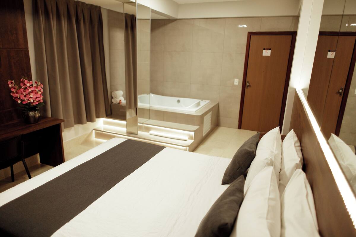 A hotel room with a bed, a desk, a mirror, a bathtub, and a door.