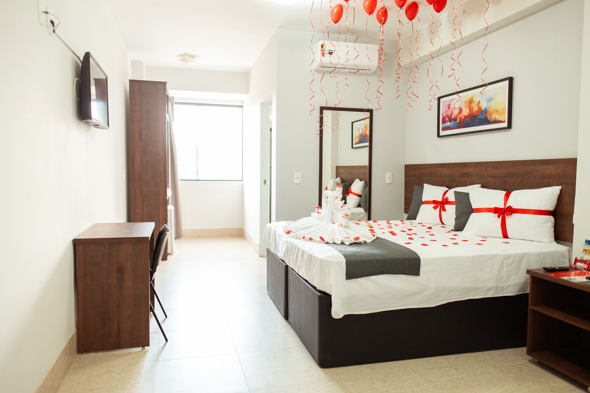 A hotel room with a bed, a desk, a chair, a wardrobe, a television, and a painting on the wall.