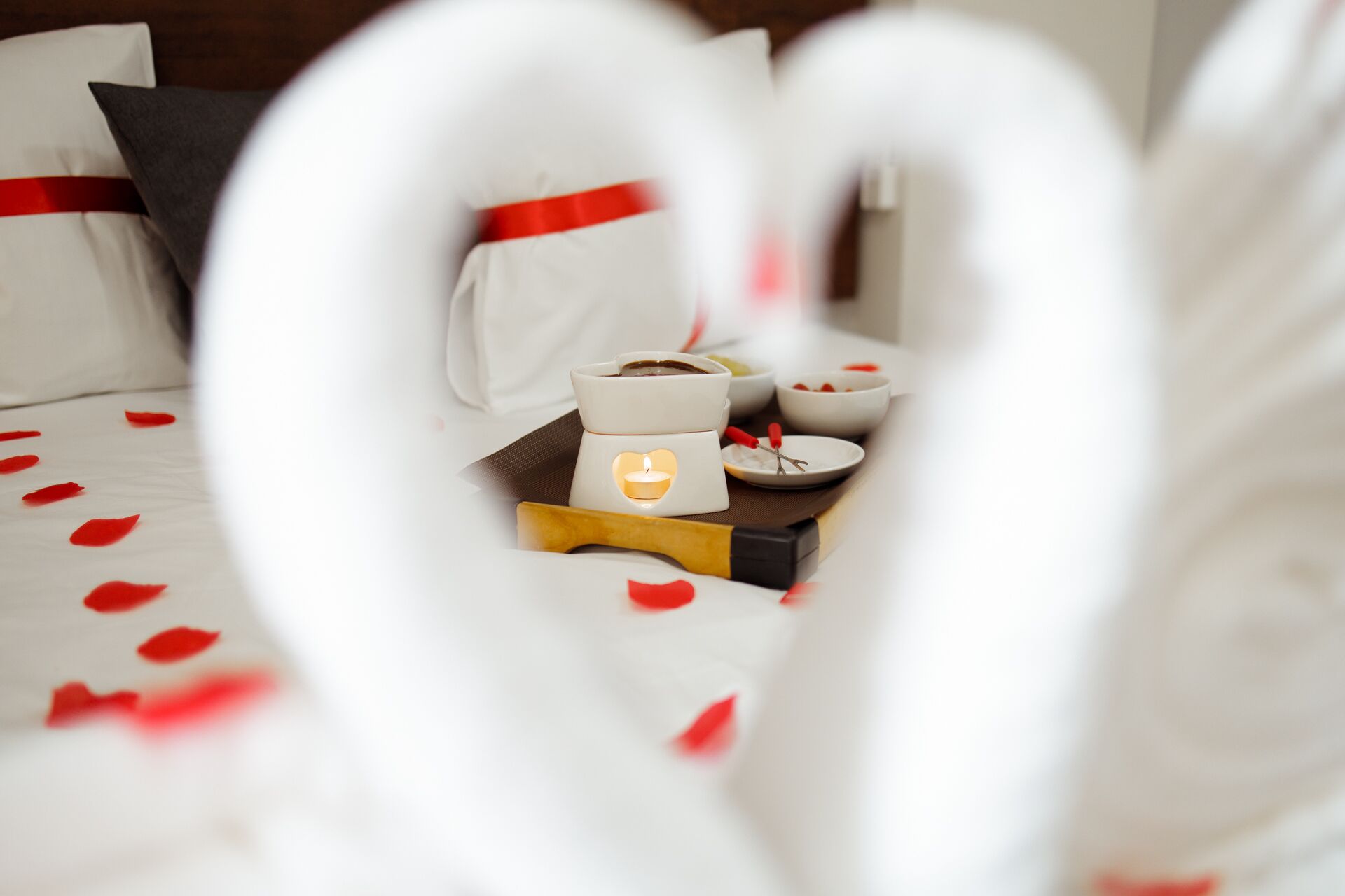 Un letto con un'accogliente composizione di cuscini bianchi a forma di cuore e un vassoio con una candela e piccole ciotole.