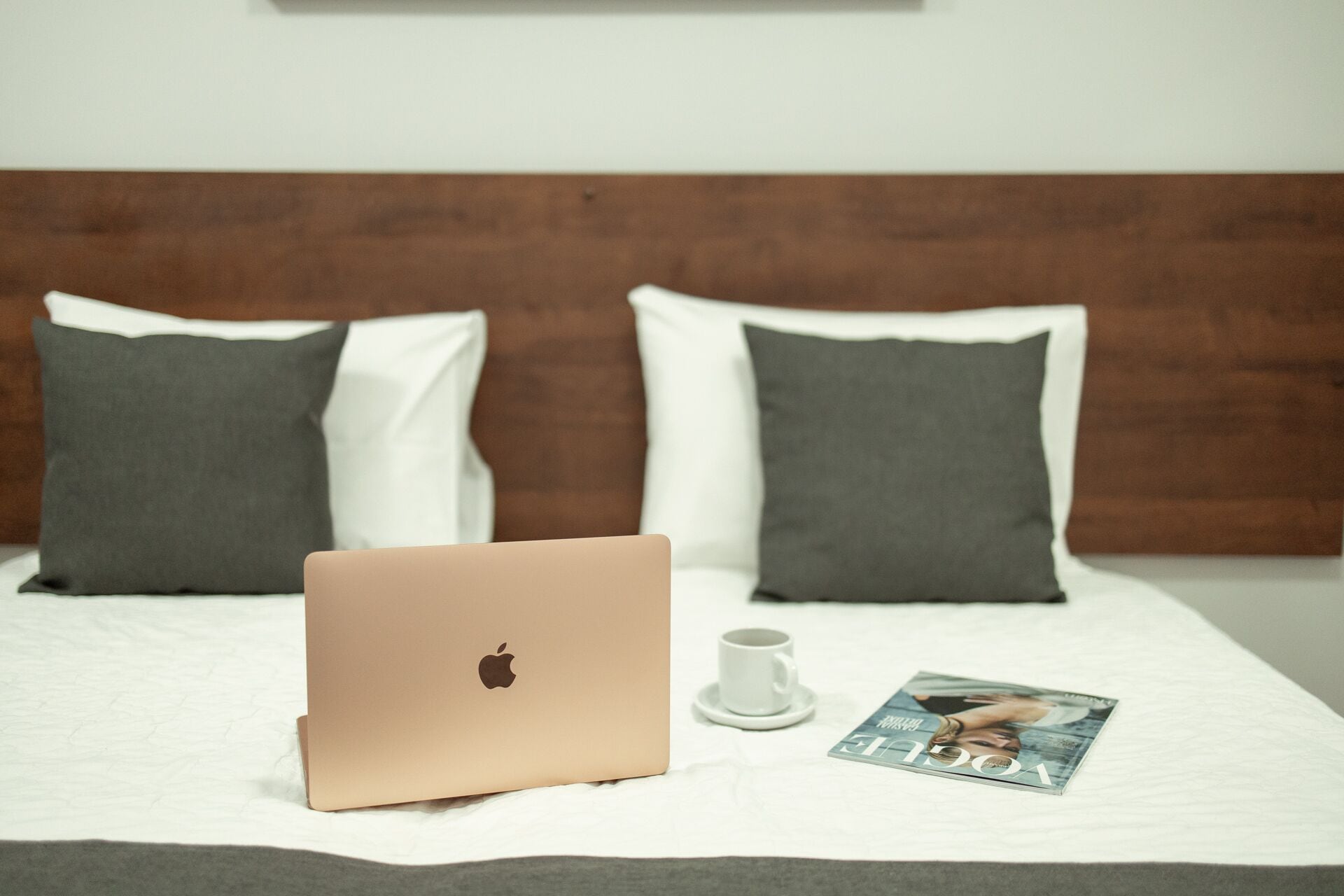 Un lit avec un ordinateur portable, une tasse blanche et un magazine posés sur un couvre-lit blanc.
