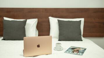 A bed with a laptop, a white mug, and a magazine on a white bedspread.