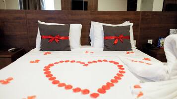 A hotel room with a neatly made bed, a heart-shaped arrangement of rose petals, and a red ribbon on the pillows.