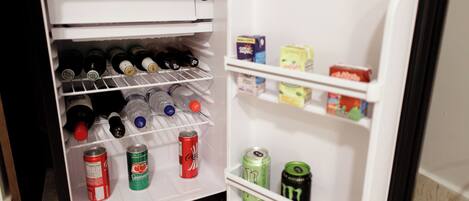 Un refrigerador abierto con repisas que contienen bebidas y aperitivos.