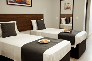 A hotel room with two single beds, each with a white bedspread and a dark-colored pillow. There is a small table with a plate of food and a drink. - Roma Hotel by H Hotéis - Airport (Arniqueiras)