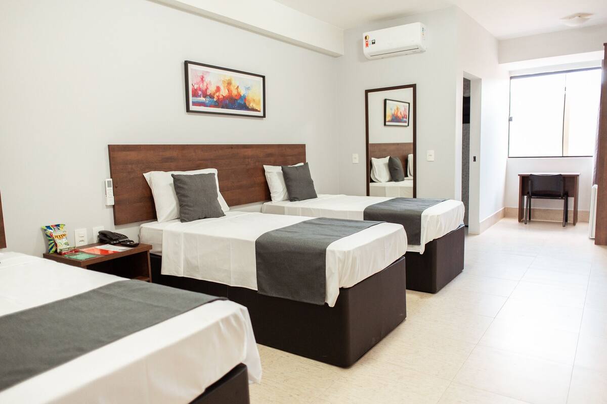 A hotel room with three beds, a desk, and a chair.