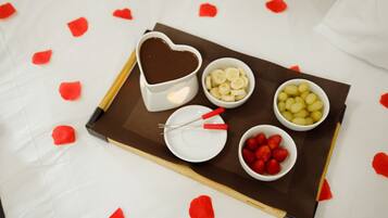 Ein Tablett mit einer Schokoladen-Tasse, Bananenscheiben, Trauben, Erdbeeren und einem kleinen weißen Teller mit Gabel und Löffel.