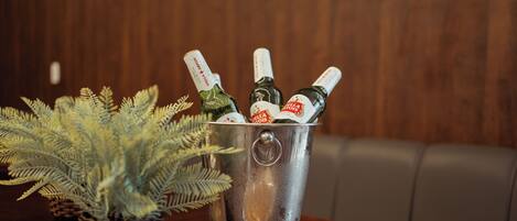A metal bucket with bottles, a plate of pastries, and a fern plant on a wooden table.