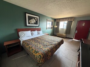 Habitación de hotel con una cama grande, una mesita de noche, un escritorio, una silla, un cuadro en la pared y una ventana con cortinas.