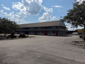 A two-story motel with a parking lot, red doors, and a clear sky.