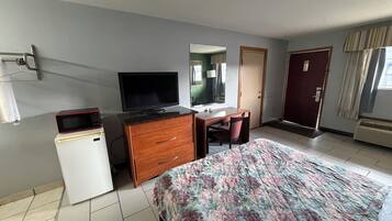 Habitación de hotel con cama, escritorio, televisión, refrigerador pequeño y puerta.