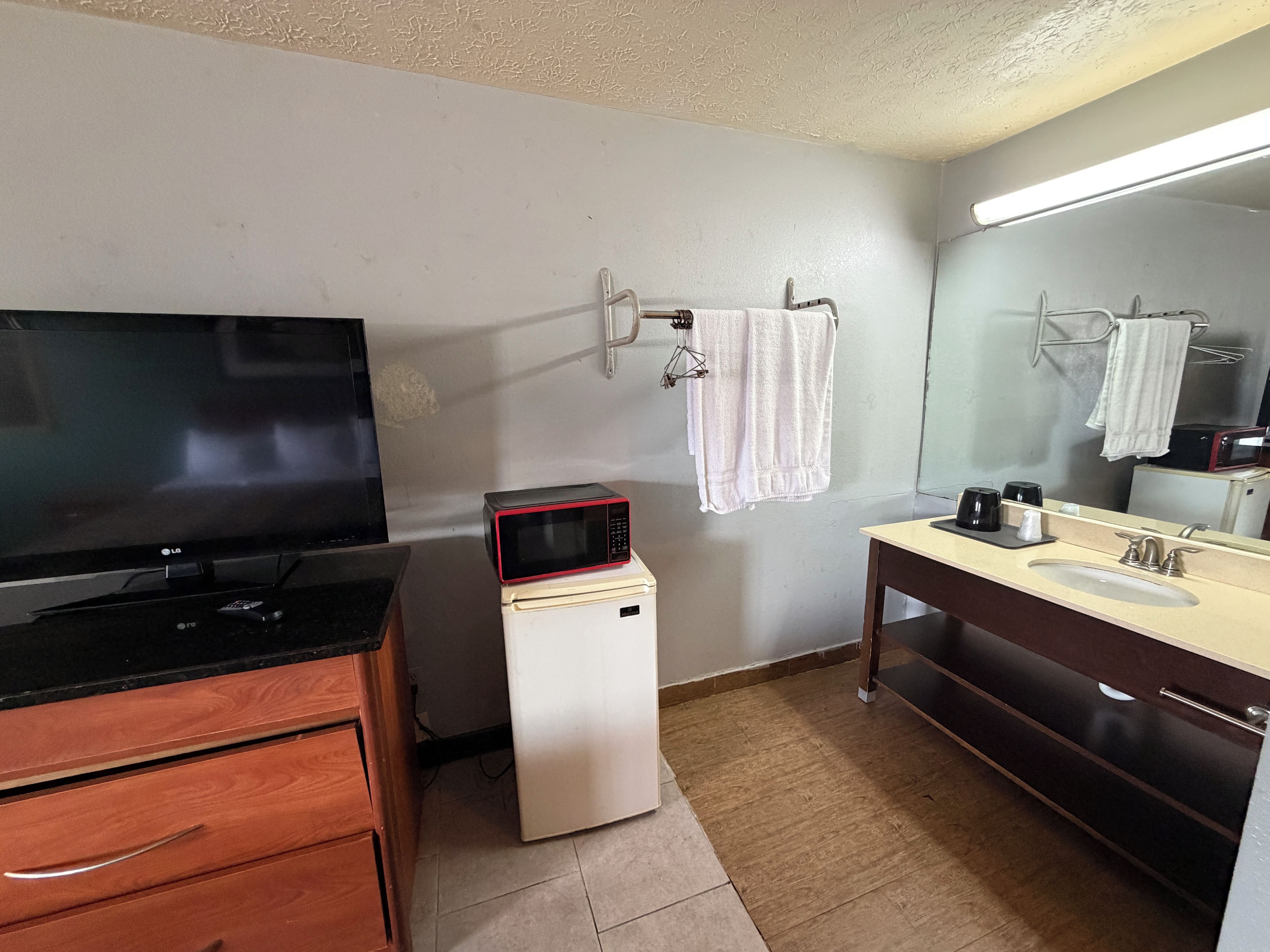 A small bathroom with a sink, mirror, towel rack, and a microwave on a small white appliance.