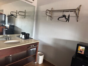 A bathroom with a sink, mirror, towel rack, and a microwave.