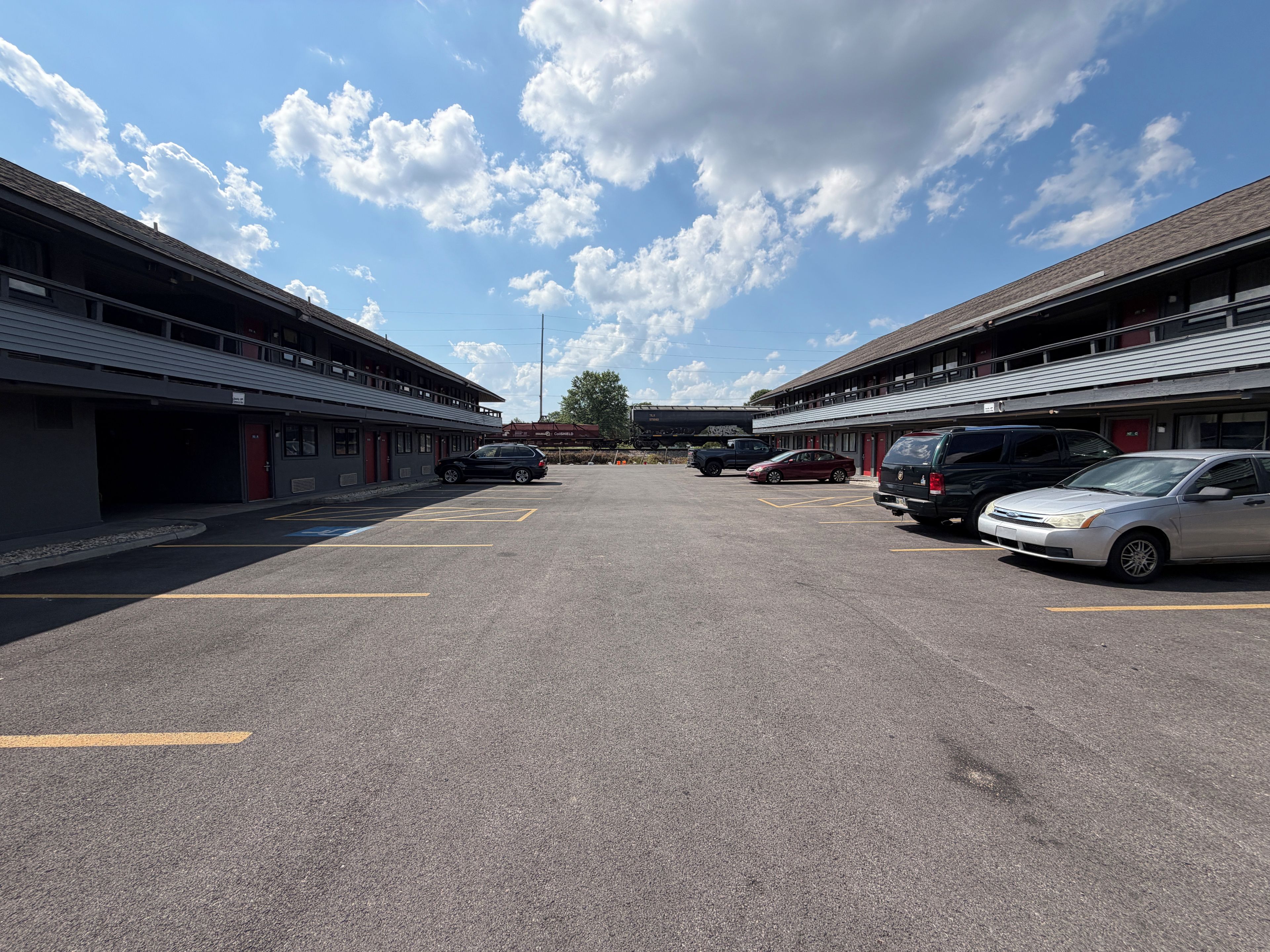 A parking lot with multiple cars and a building with a flat roof and large windows.