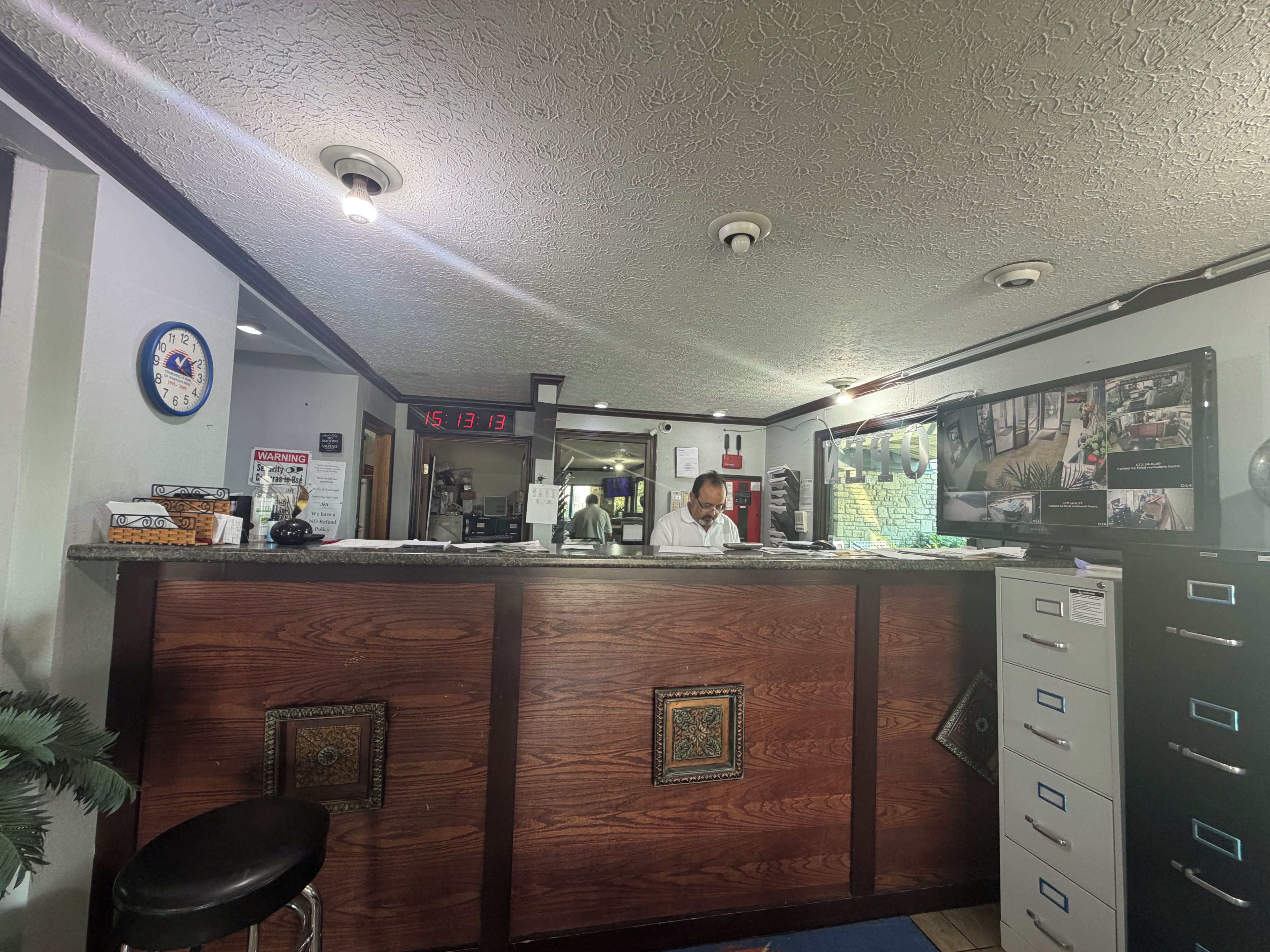 A reception desk with a clock, a digital display, and a security camera monitor.