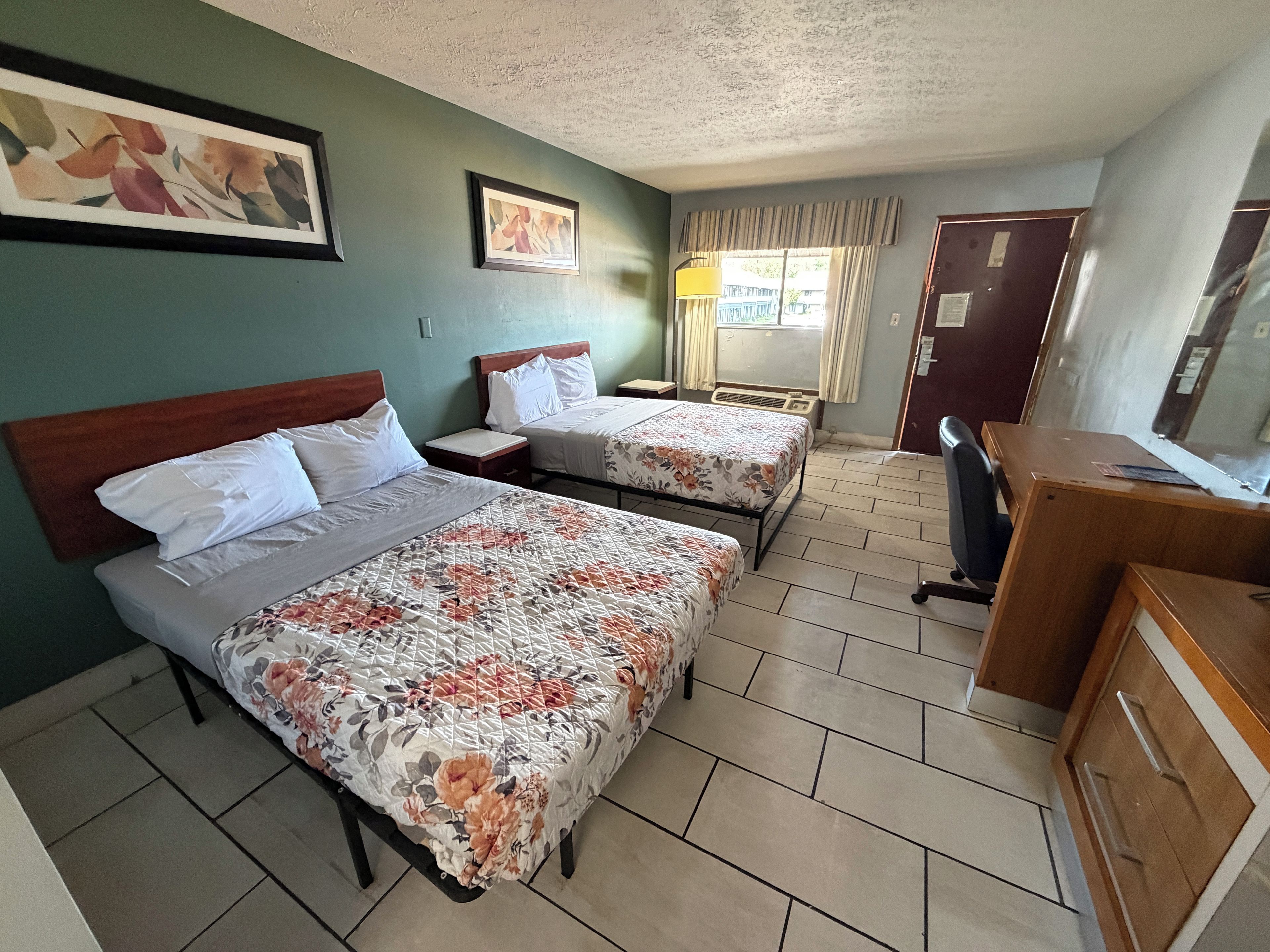 A hotel room with two beds, a desk, a chair, and a window with curtains.