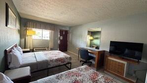 Una camera d'albergo con due letti, una scrivania, un televisore e una porta.