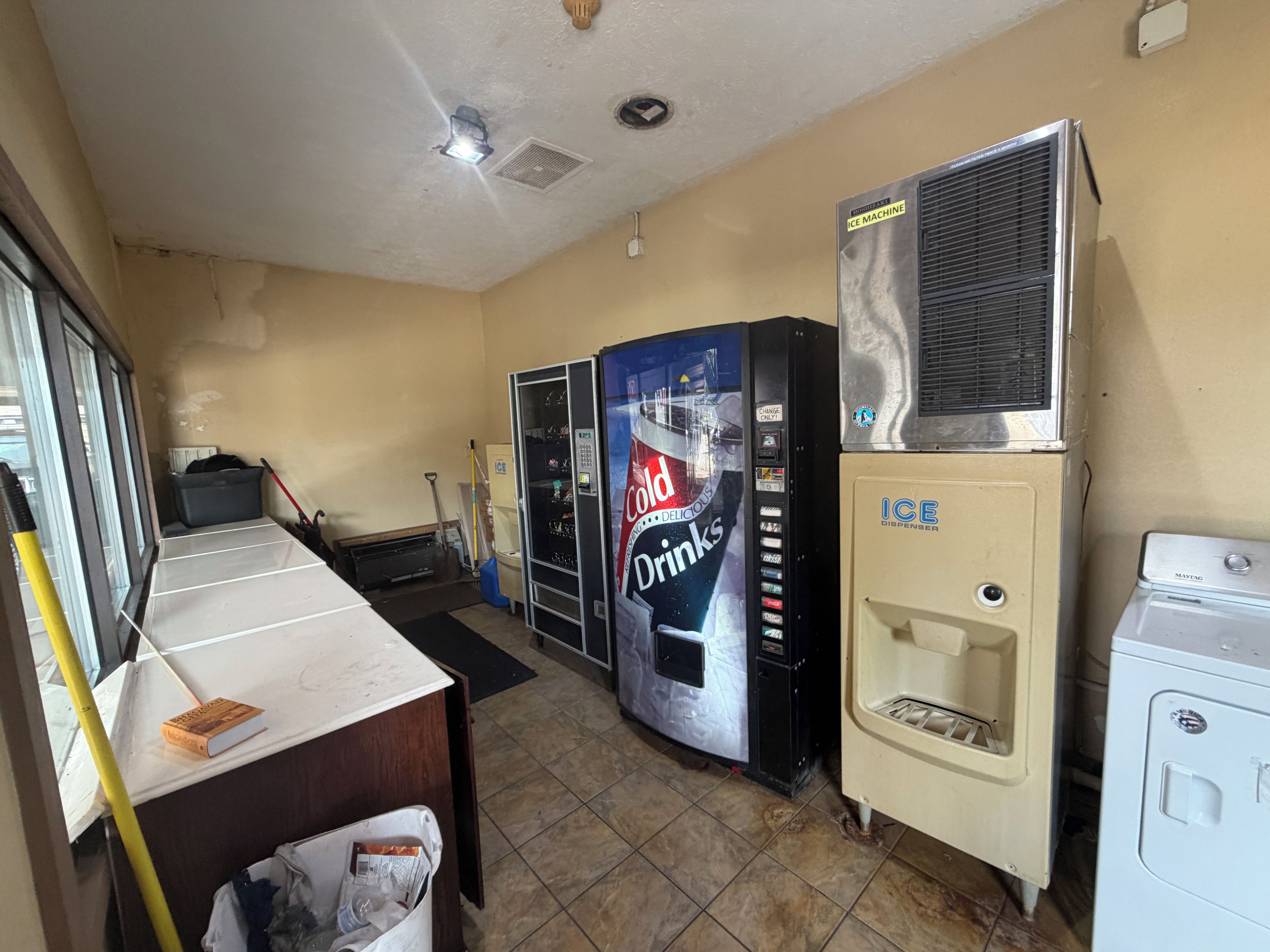 A room with a vending machine, an ice dispenser, and a window with blinds.
