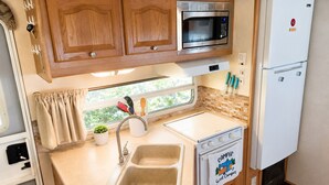 Una kitchenette compacta con armarios de madera, un microondas, un refrigerador, un fregadero y una estufa.