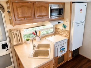 A compact kitchenette with wooden cabinets, a microwave, a refrigerator, a sink, and a stove.