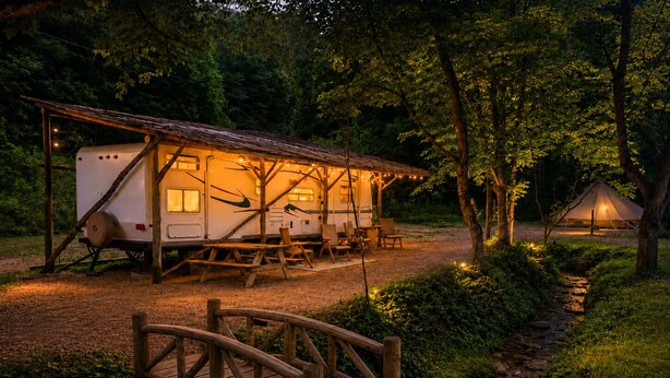 Un camping con una caravana techada, mesas de picnic y un puente de madera.