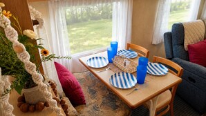 Interior acogedor de una caravana con una mesa de comedor para cuatro personas, platos y tazas azul rayado, una cesta de mimbre y una planta en maceta.