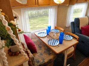 A cozy RV interior with a dining table set for four, surrounded by blue-striped plates and cups, a wicker basket, and a potted plant.