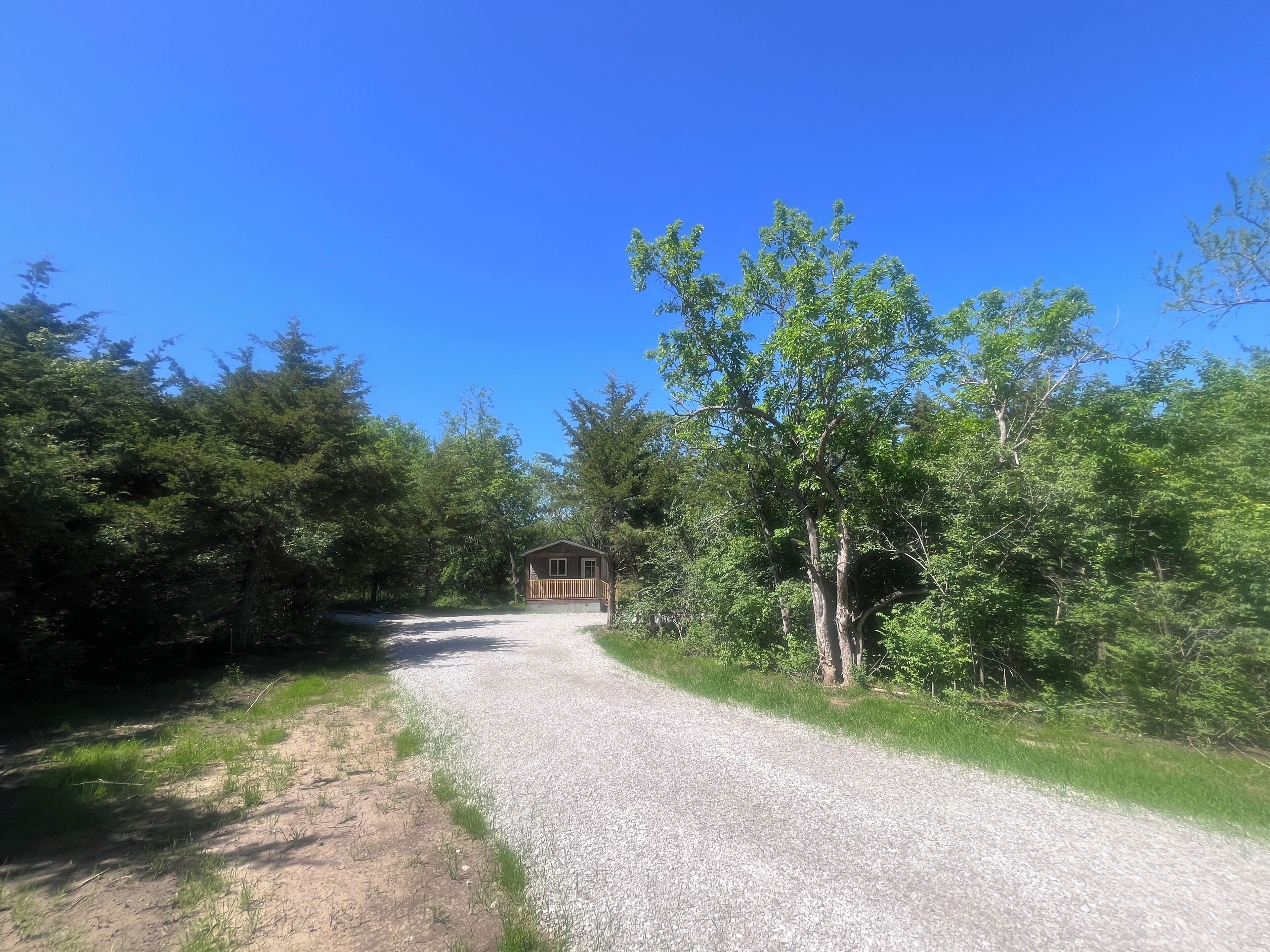 Un sentier de gravier mène à un chalet en bois, entouré d’une forêt dense.