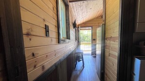 A narrow hallway with wooden walls and a wooden ceiling. There is a window on the left, a stool in the middle, and a refrigerator on the right. - Quiet Cabin in the woods.  (Williamsburg)