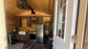 A compact kitchen with wooden cabinets, a microwave, and a refrigerator. - Quiet Cabin in the woods.  (Williamsburg)