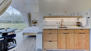 Un dormitorio moderno y minimalista con una cama de madera, una mesita de noche pequeña y vistas a un paisaje verde exuberante a través de amplios ventanales.
