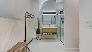 Un baño moderno con un banco de madera, un espejo, un lavabo con tocador de madera y un box de ducha de vidrio.