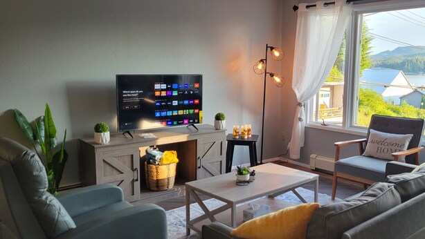 En moderne stue med fjernsyn, sofa, lænestol og havudsigt.