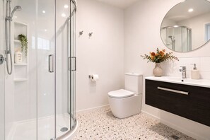 Ein modernes Badezimmer mit Duschkabine aus Glas, Toilette, Waschtisch mit Spiegel und einer dekorativen Vase mit Blumen.