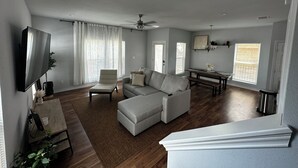 Un salon spacieux avec un canapé gris, une table à manger et un téléviseur fixé au mur.