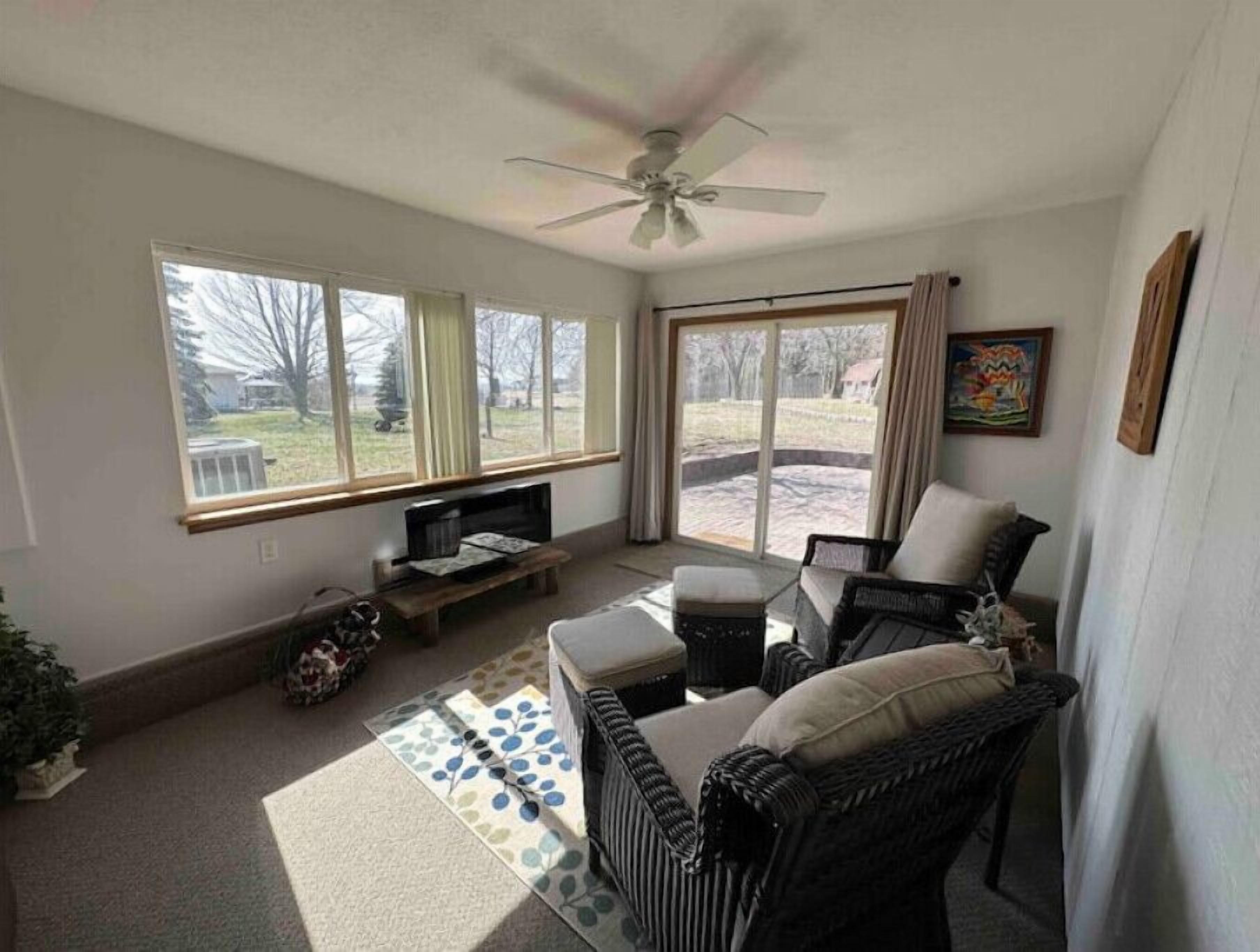 Una sala de estar con ventilador de techo, un sofá, una mesa de centro y un televisor. Hay ventanas y una puerta que da a un área exterior.