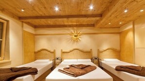 Een kamer met twee bedden, houten balkenplafond en een zonlichtarmatuur aan de muur.