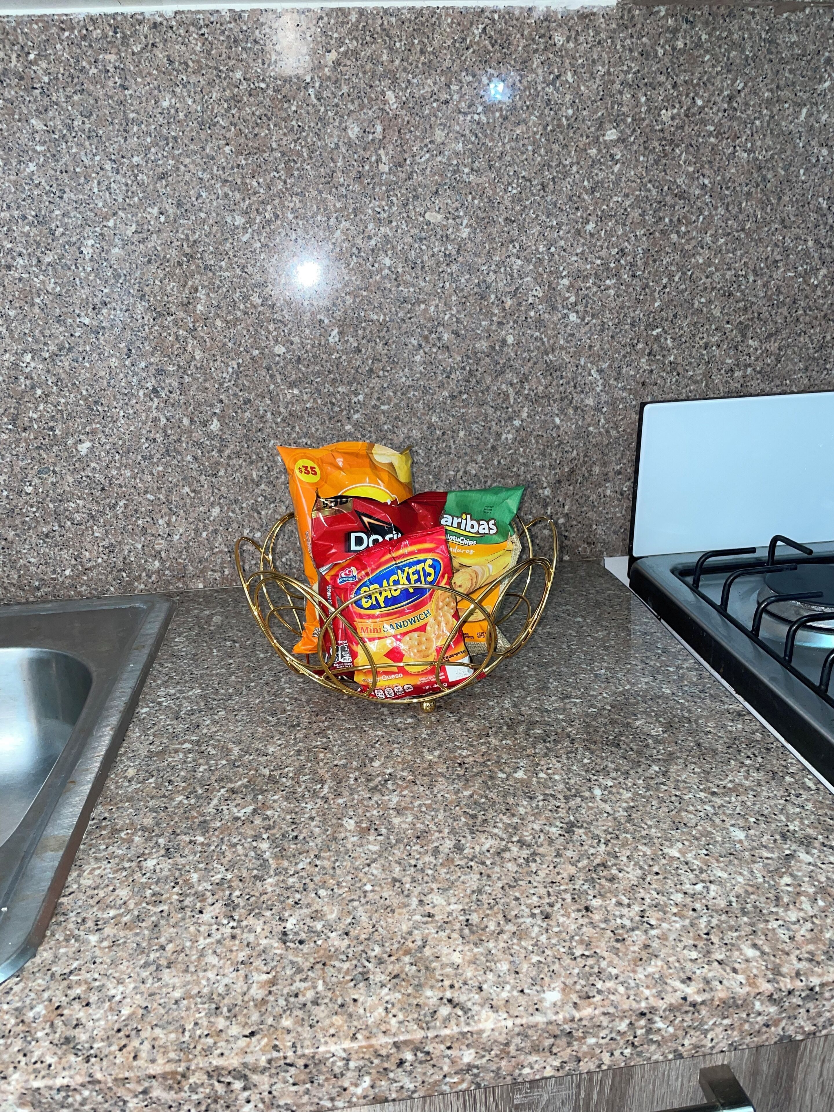 A kitchen counter with a granite backsplash, a stainless steel sink, and a gas stove.